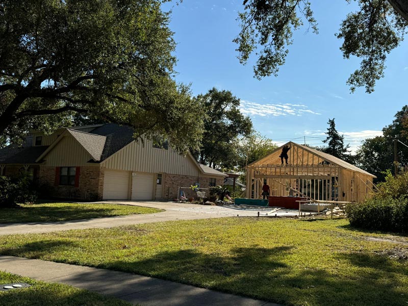 Wide view of garage construction in progress next to completed Houston home