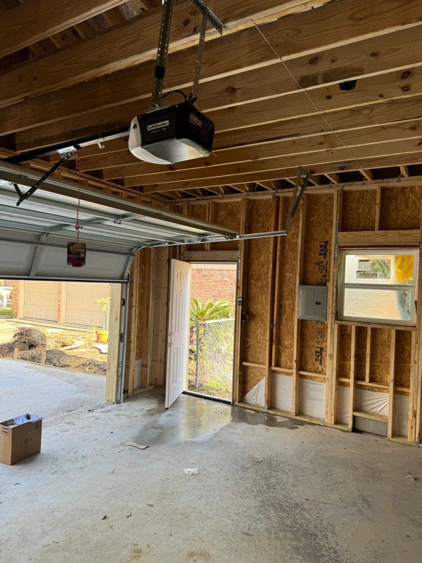 Installed garage door opener and personnel door with exposed framing in Houston garage