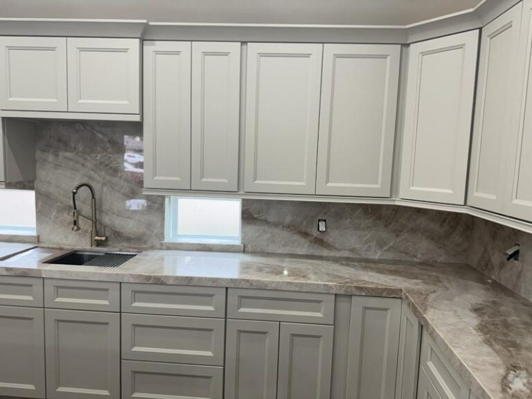Detail of gray upper cabinets, full-slab stone backsplash, brushed faucet and undermount sink - kitchen remodeling in Houston, TX