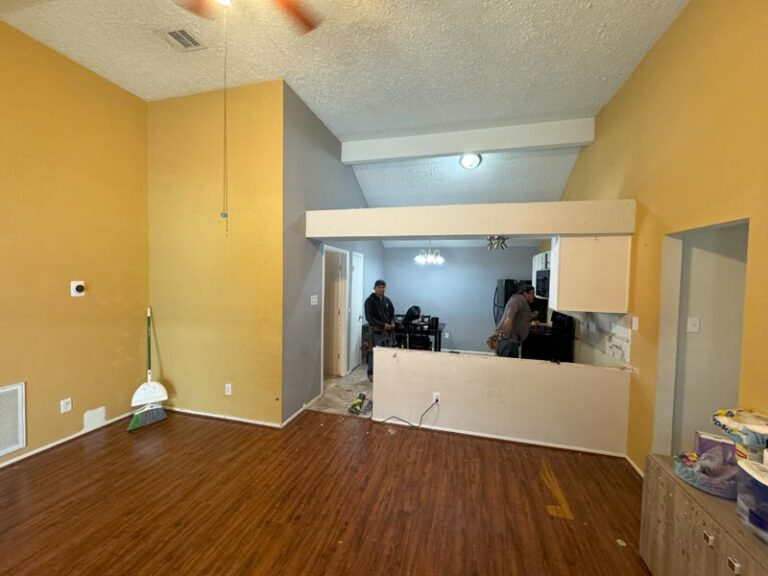 Dated yellow-walled dining area with half wall and old laminate flooring before remodel - kitchen remodeling in Houston, TX