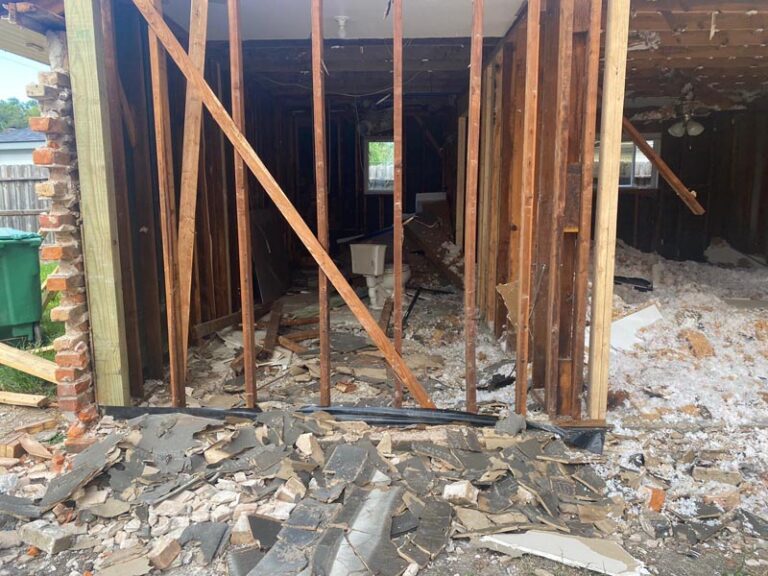 Demolition phase with exterior wall opened to exposed wood stud framing and debris on the slab - in-law suite addition in Houston, TX