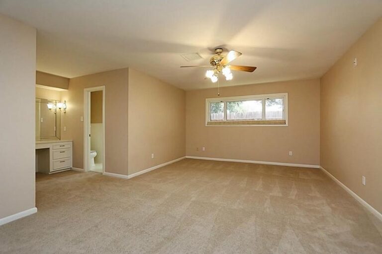 Original beige carpeted bedroom with dated ceiling fan and small window before the suite conversion - in-law suite addition in Houston, TX