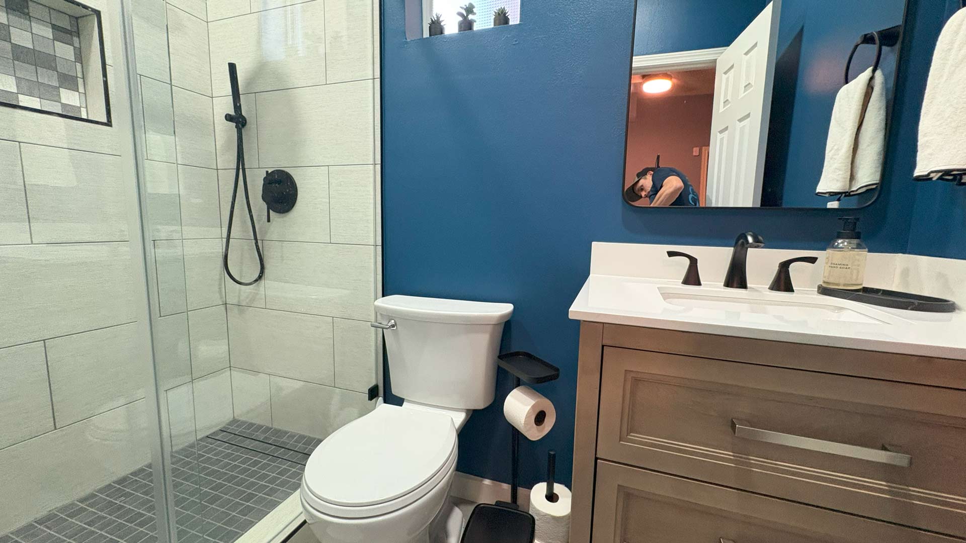 Remodeled small bathroom with tiled walk-in shower, blue accent walls, and light wood vanity in Houston.