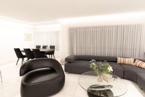 Open-concept living and dining room with black furniture and LED cove lighting in Houston remodel