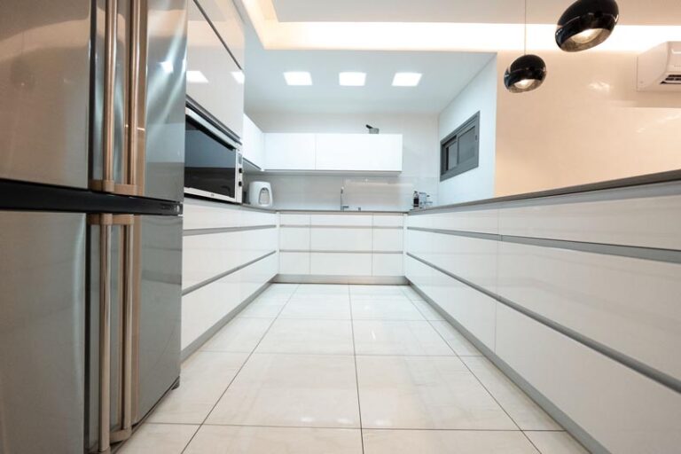 Galley view of parallel white flat-panel cabinet runs with gray countertops and recessed ceiling lighting - modern kitchen remodel in Houston, TX
