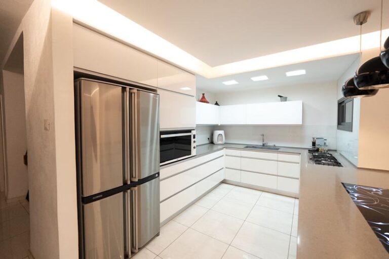 Corner view of white kitchen with double stainless refrigerator, built-in microwave, and recessed ceiling light box - modern kitchen remodel in