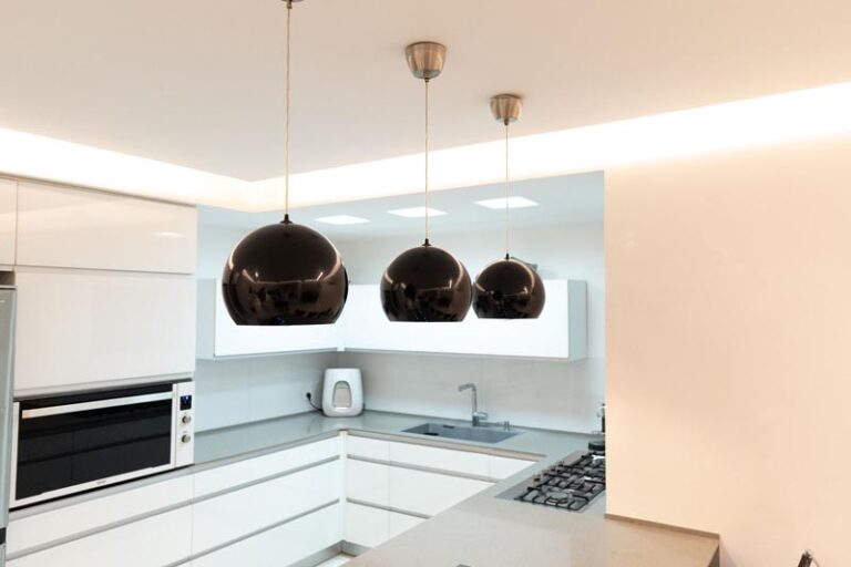 Three black globe pendant lights over the kitchen counter with white cabinetry and backlit ceiling - modern kitchen remodel in Houston, TX