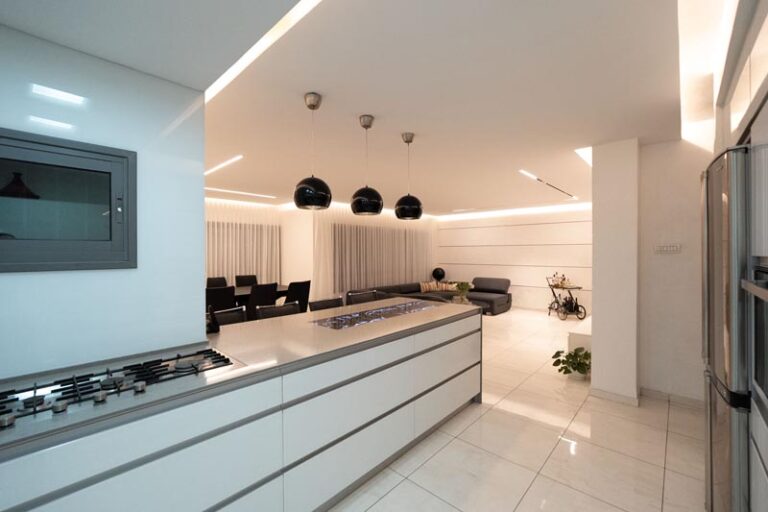 Kitchen counter with built-in stainless gas cooktop under black pendants, opening to the living area - modern kitchen remodel in Houston, TX