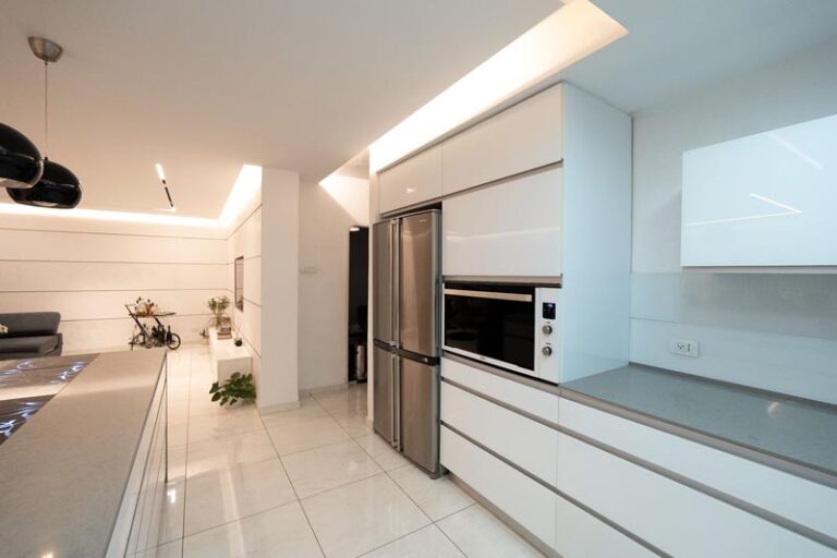 Kitchen appliance wall with stainless refrigerator and built-in oven flanked by glossy white cabinetry - modern kitchen remodel in Houston, TX