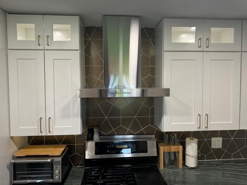 Stainless steel range hood and geometric backsplash detail in affordable Houston kitchen builders project