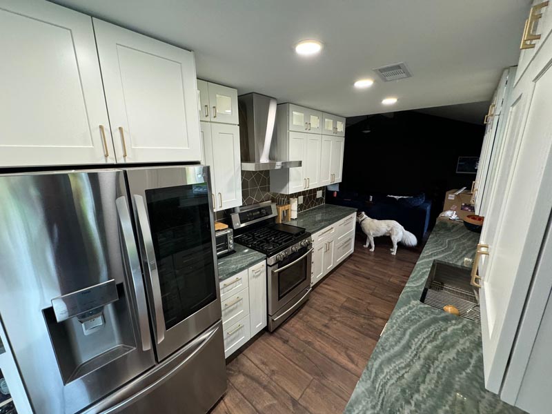 Full kitchen renovation Houston featuring stainless appliances white cabinetry and wood-look vinyl flooring