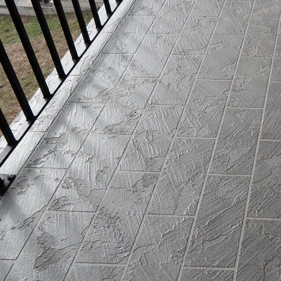 Textured waterproof balcony coating beside a black metal railing with lawn beyond in Seabrook, TX