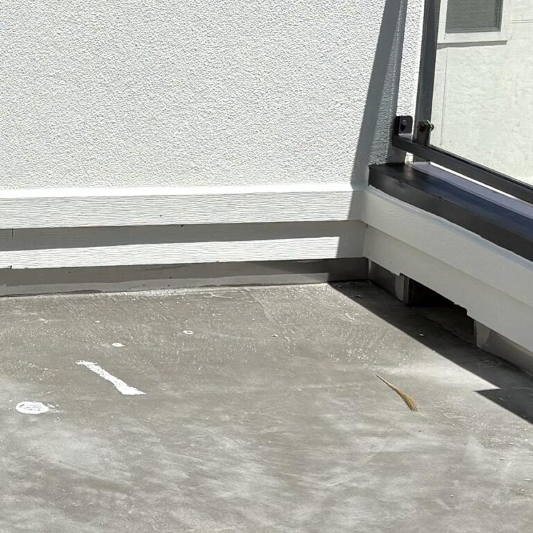 Balcony stripped to bare concrete substrate along glass railing base and white stucco wall before new waterproofing, 77007 site