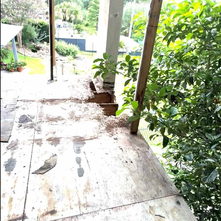 Balcony deck stripped to bare plywood subfloor at support columns during demolition, 77586 site