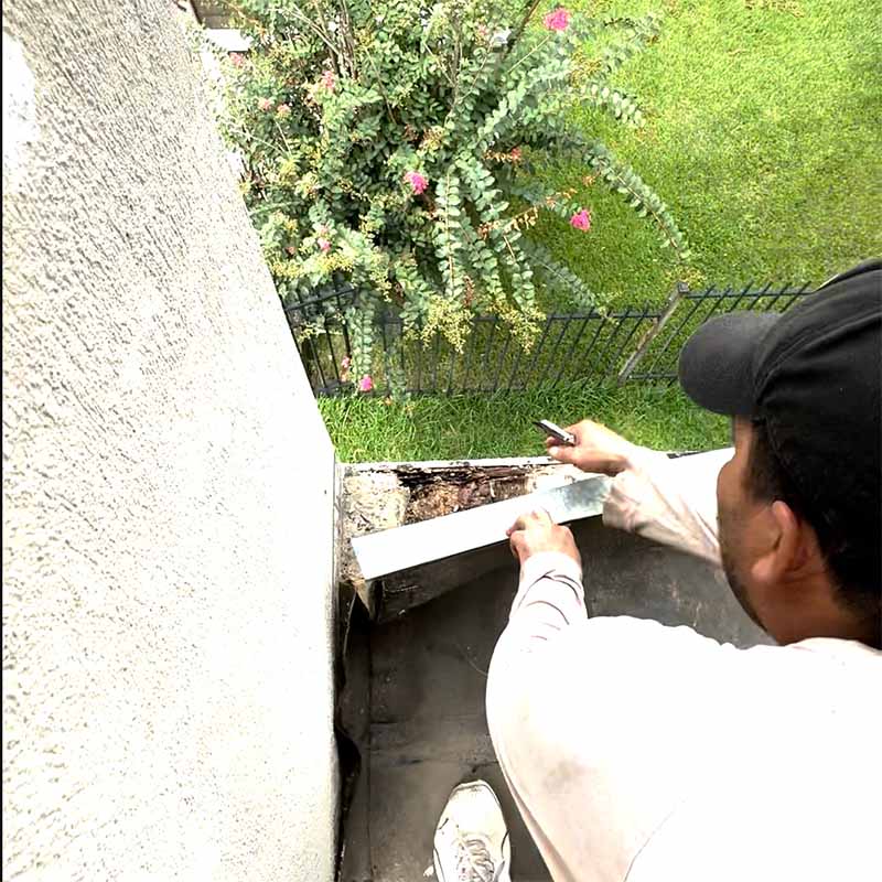 Contractor working on damaged balcony edge flashing above a landscaped yard in Seabrook, TX