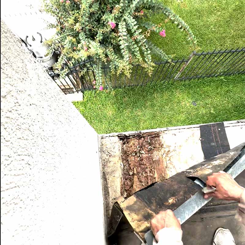 Worker prying old metal drip-edge flashing from a rotted balcony edge in Seabrook, TX