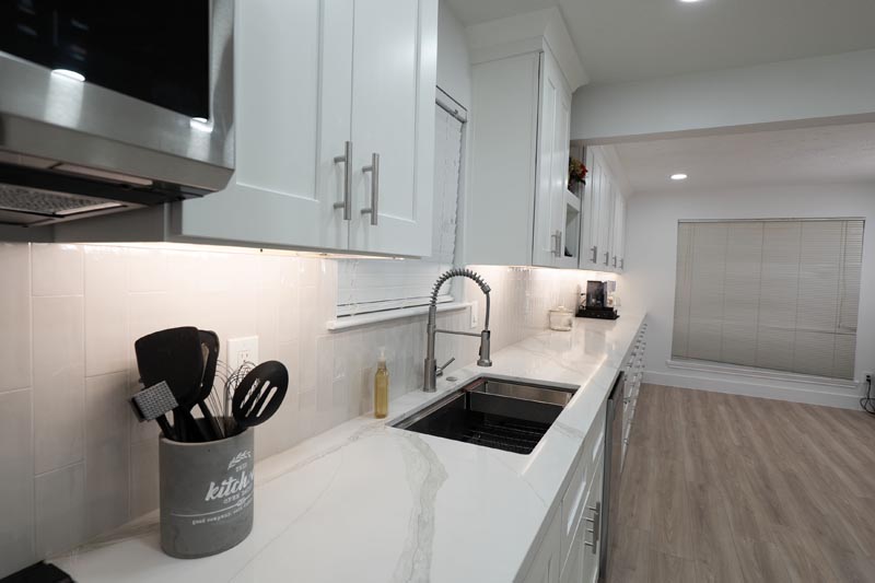 Commercial-style kitchen faucet with white subway tile backsplash and under-cabinet lighting