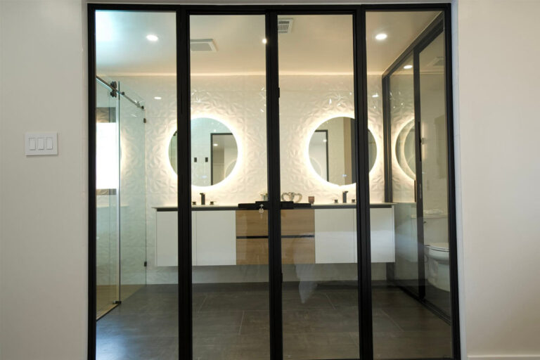 Black-framed glass partition doors from bedroom opening onto remodeled bathroom with dual backlit mirrors and floating vanity - condo bathroom