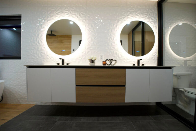 Double floating vanity with two round backlit LED mirrors against sculpted 3D white tile wall - condo bathroom remodeling in Houston, TX