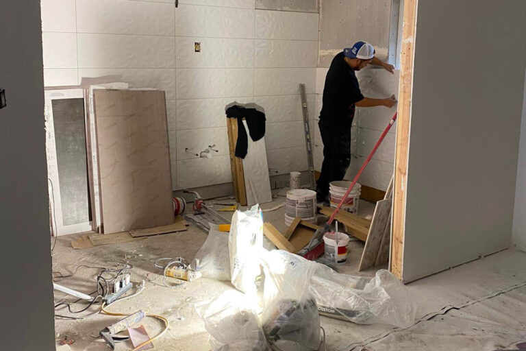 Installer setting white 3D textured wall tile from a work platform amid construction materials - condo bathroom remodeling in Houston, TX