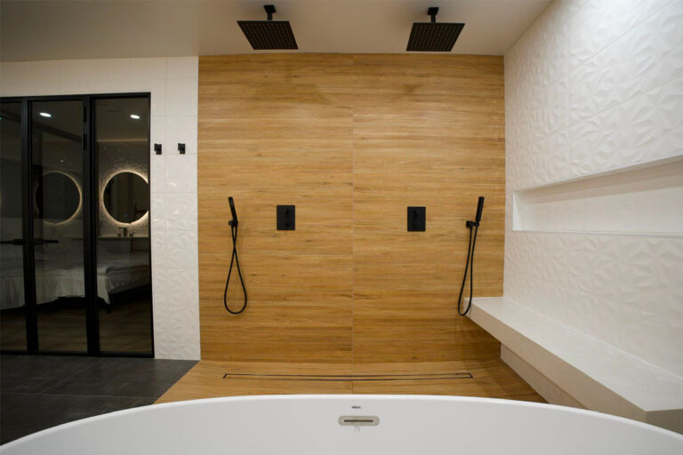 Completed walk-in shower wall with two matte-black rain showerheads, hand sprayers, linear drain and floating bench - condo bathroom remodeling