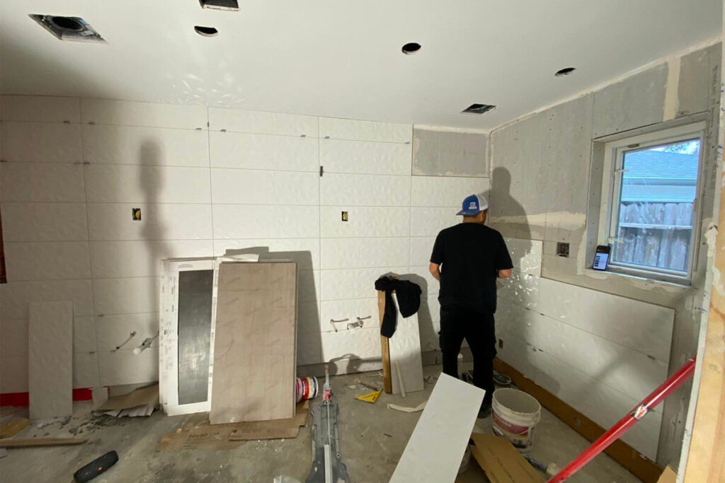 Contractor installing large-format wall tile with recessed niche during permitted condo bathroom renovation