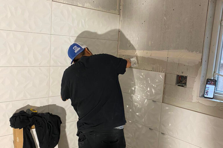 Close-up of tile setter fitting textured white wall tile panels in the condo bathroom - condo bathroom remodeling in Houston, TX